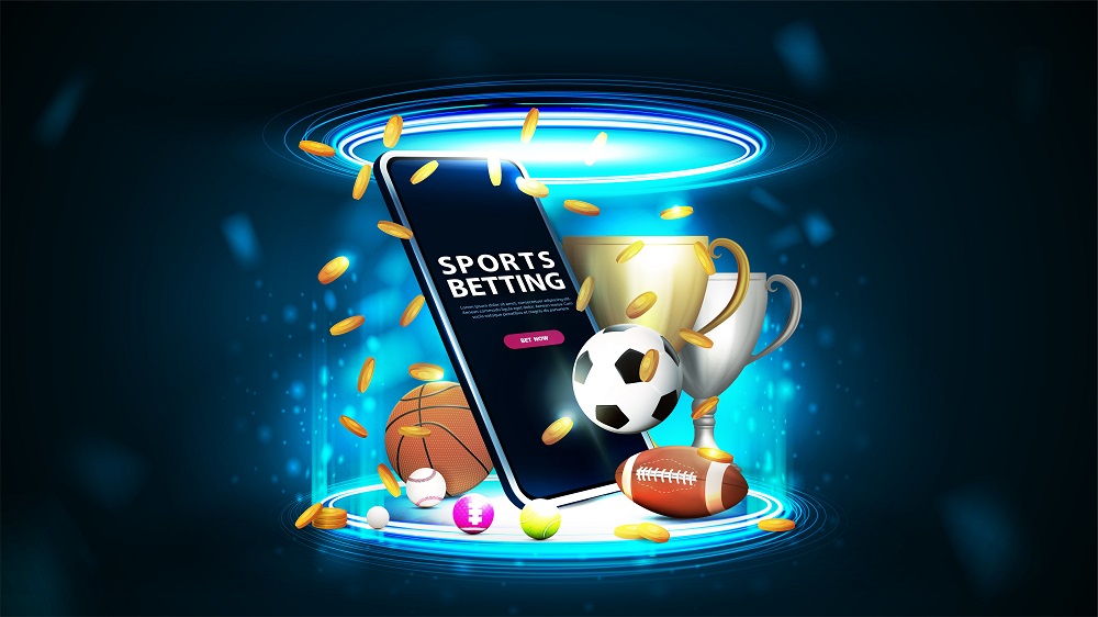 Smartphone under the spotlight with Sports Betting text on its' screen, surrounded by different types of sport equipment and trophies.